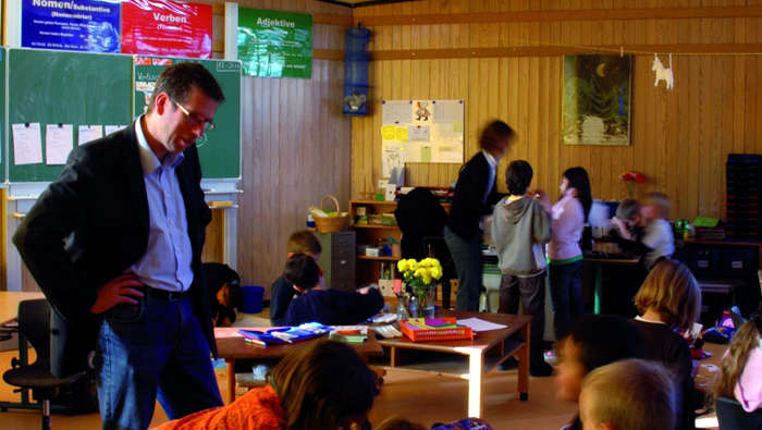 Um professor ajuda os alunos em In der Alten Forst, iluminada pela iluminação escolar Philips