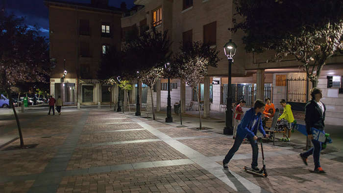 Crianças a brincar à noite numa praça iluminada com iluminação Philips