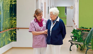 Enfermeira a cuidar de uma senhora idosa num corredor iluminado