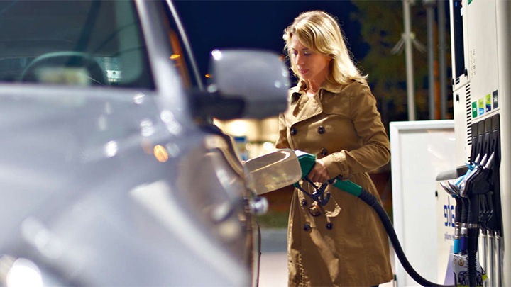 Uma mulher abastece o depósito do carro num posto de combustível sob as luzes brilhantes da iluminação da cobertura da Philips.