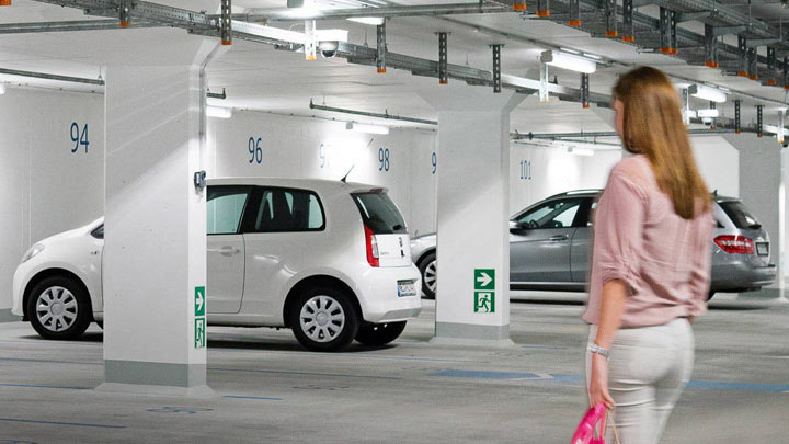 Uma mulher caminha para o carro num parque de estacionamento subterrâneo bem iluminado 