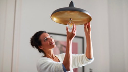 Mulher a enroscar uma lâmpada de venda ao consumidor em casa	