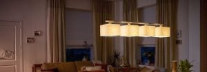 Candeeiro suspenso LED com vários tons de tecido ilumina uma acolhedora sala de estar, apresentando soluções de iluminação para casa elegantes e energeticamente eficientes para o conforto noturno.
