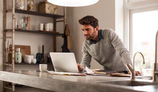 Homem a utilizar um computador portátil num escritório em casa bem iluminado com iluminação LED de trabalho para uma configuração de teletrabalho eficiente.