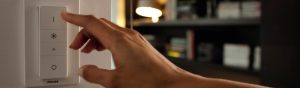 "Ajuste manual do dimmer para LED inteligente da Philips, controlando a iluminação ambiente numa acolhedora sala de estar com estantes."