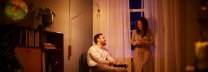 "Candeeiro de pé com lâmpada LED de estilo vintage que cria um ambiente acolhedor para a conversa ao entardecer de um casal, apresentando uma iluminação ambiente energeticamente eficiente numa sala de estar acolhedora."
